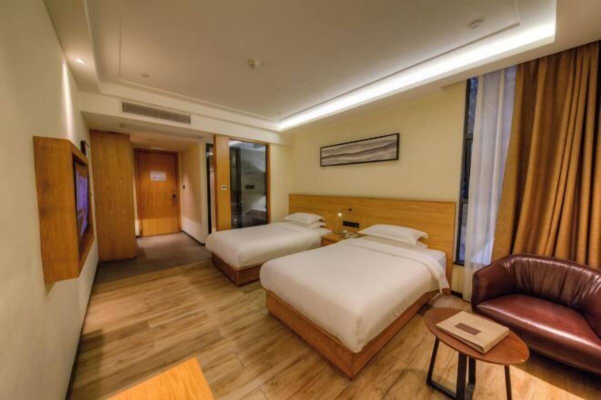 A hotel room with two beds, a leather sofa, a small table, and a painting on the wall.
