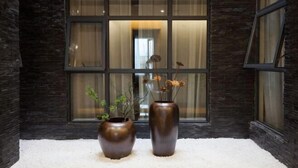 Deux grands vases remplis de fleurs séchées sont placés devant une fenêtre ornée de rideaux.