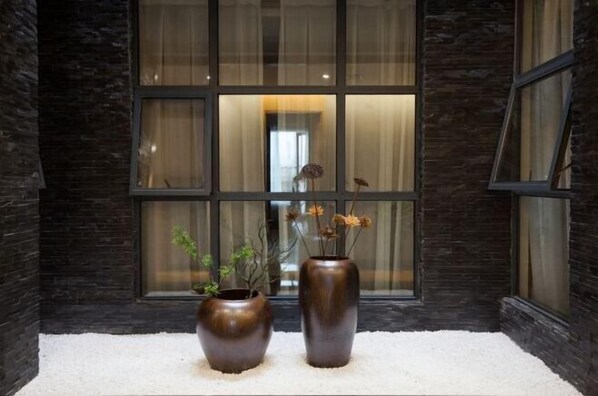Deux grands vases remplis de fleurs séchées sont placés devant une fenêtre ornée de rideaux.