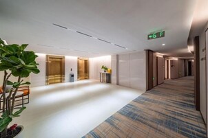 A hotel corridor with a carpeted floor, a reception desk, and a plant.