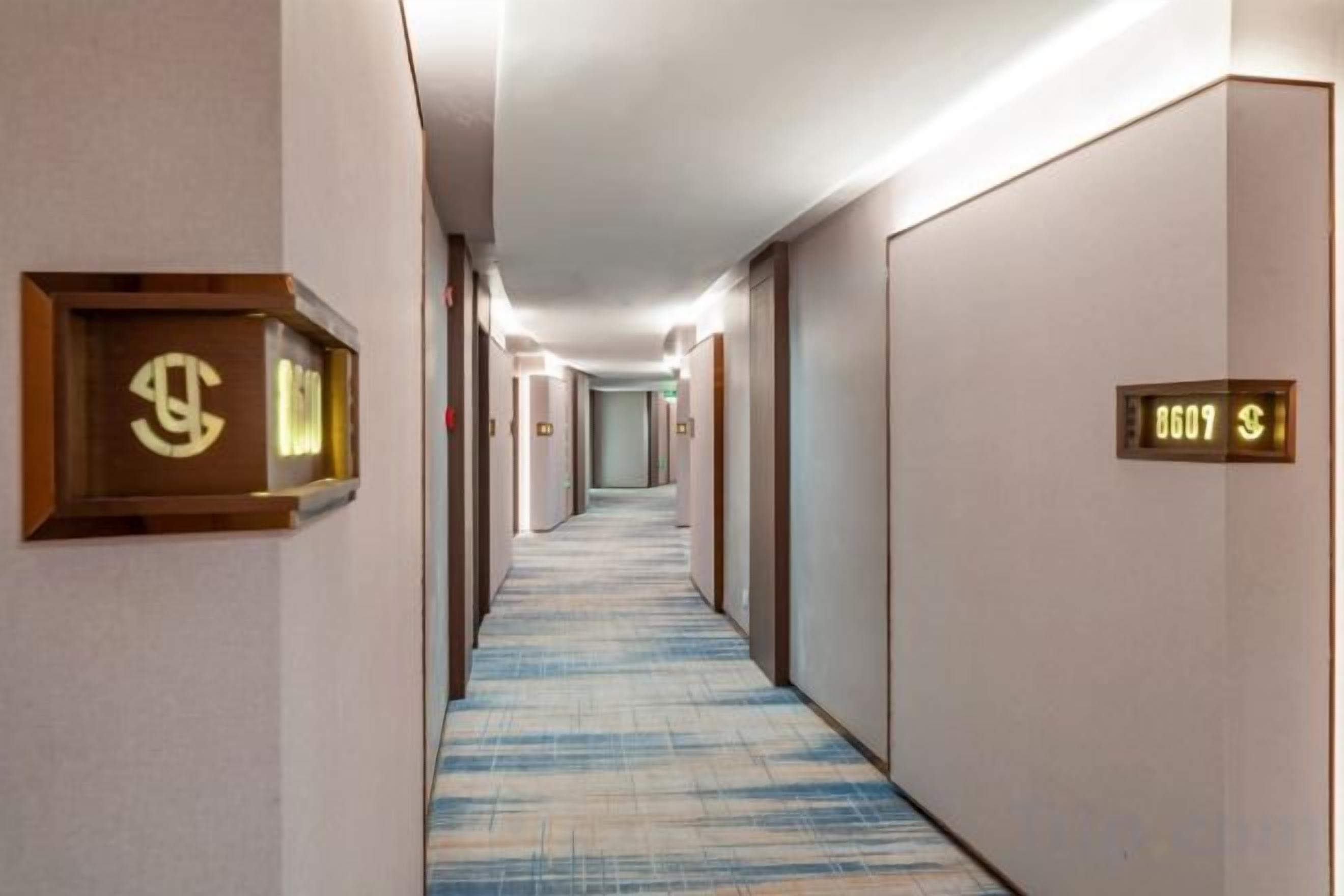 A hotel hallway with carpeted floors, doors with room numbers, and a light fixture on the ceiling.