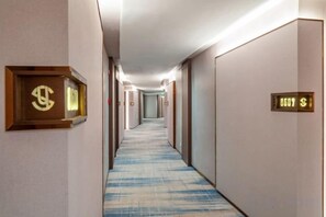 A hotel hallway with carpeted floors, doors with room numbers, and a light fixture on the ceiling. - Yearnsun Hotel (Taicang)