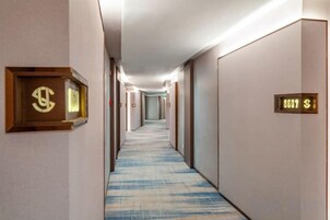 Un pasillo de hotel con pisos alfombrados, puertas con números de habitación y un accesorio de iluminación en el techo.