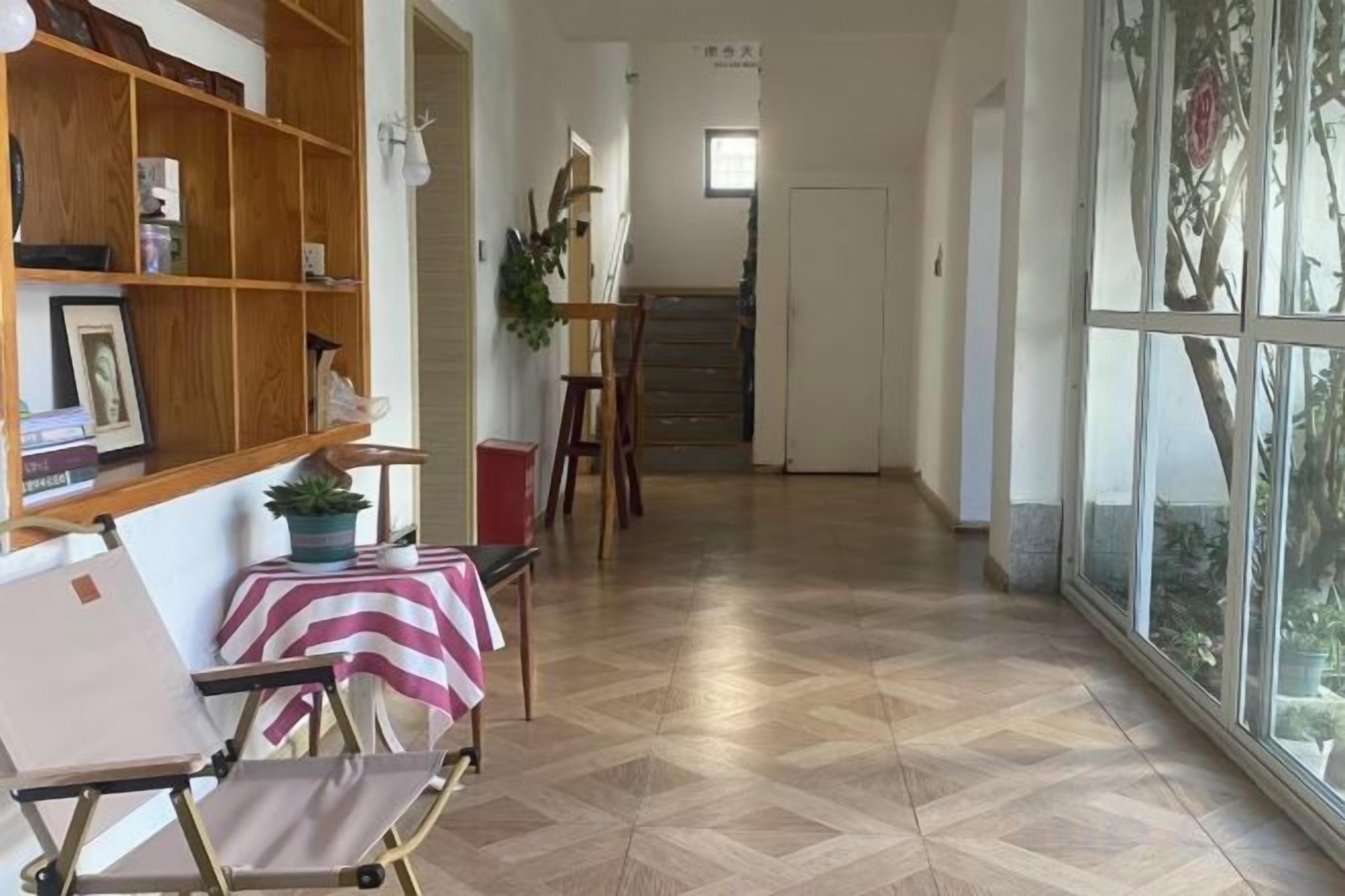Un pasillo con piso de madera, una silla con mantel a rayas, una estantería y un ventanal con vistas.