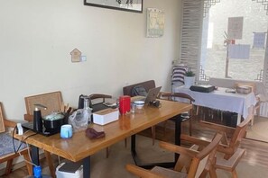 Uma área de refeições com mesa de madeira, cadeiras e diversos objetos, como uma cafeteira, xícaras e um laptop.