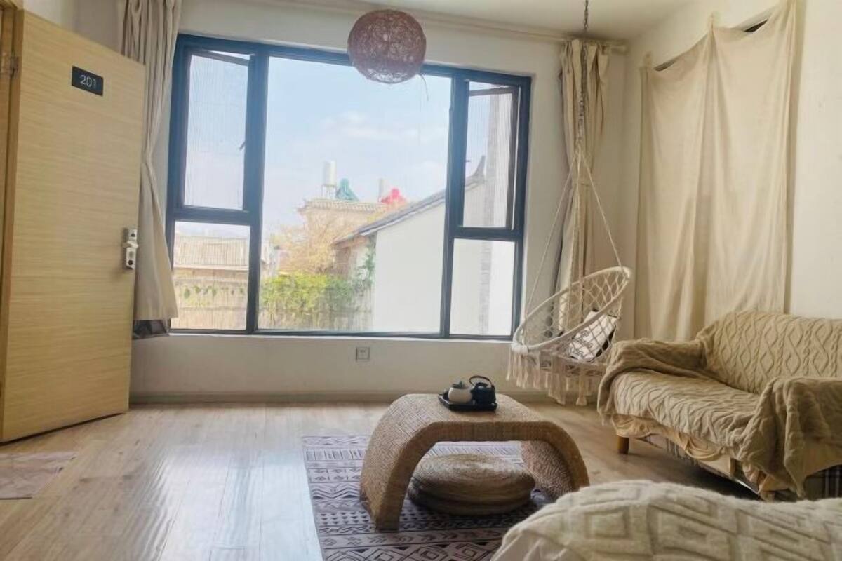 A room with a large window, a sofa, a hanging chair, a small table, and a door labeled '201'.