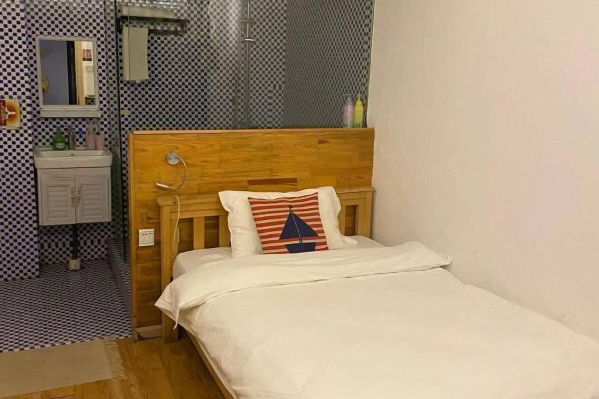 A small, neatly made bed with a wooden headboard, a white bedside table, and a mirror above it.