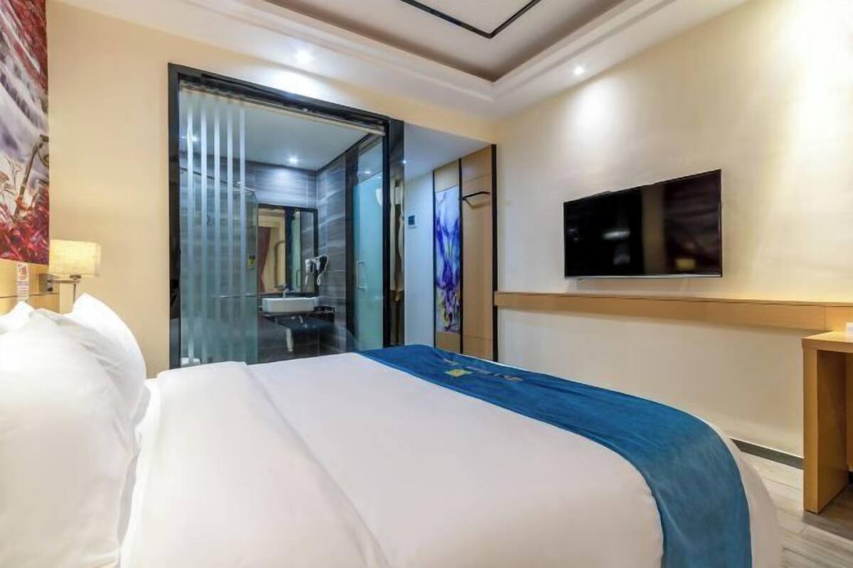 Une chambre d’hôtel équipée d’un lit, d’une télévision, d’un miroir et d’une salle de bain visible à travers une porte en verre.