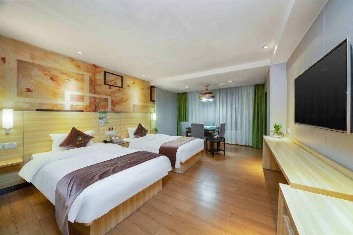 Une chambre d’hôtel avec deux lits, un bureau, une chaise, une télévision et une grande fenêtre avec des rideaux.