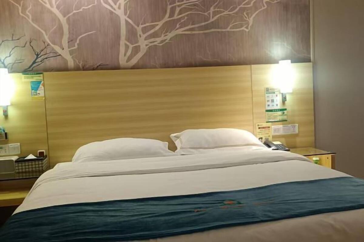Une chambre d’hôtel avec une tête de lit en bois, un lit avec une literie blanche, une table de chevet avec une lampe et un téléphone fixé au mur.