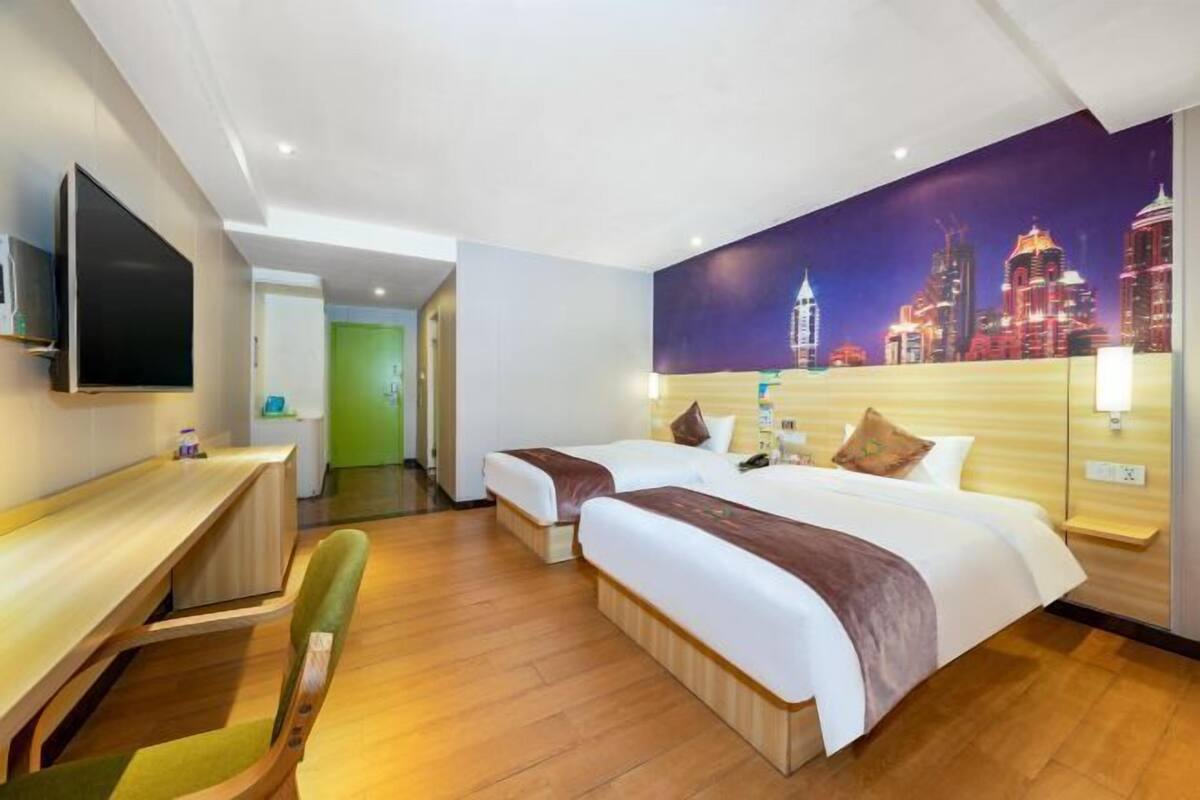 Une chambre d’hôtel avec deux lits, un bureau, une chaise, un téléviseur et une fresque représentant un paysage urbain sur le mur.