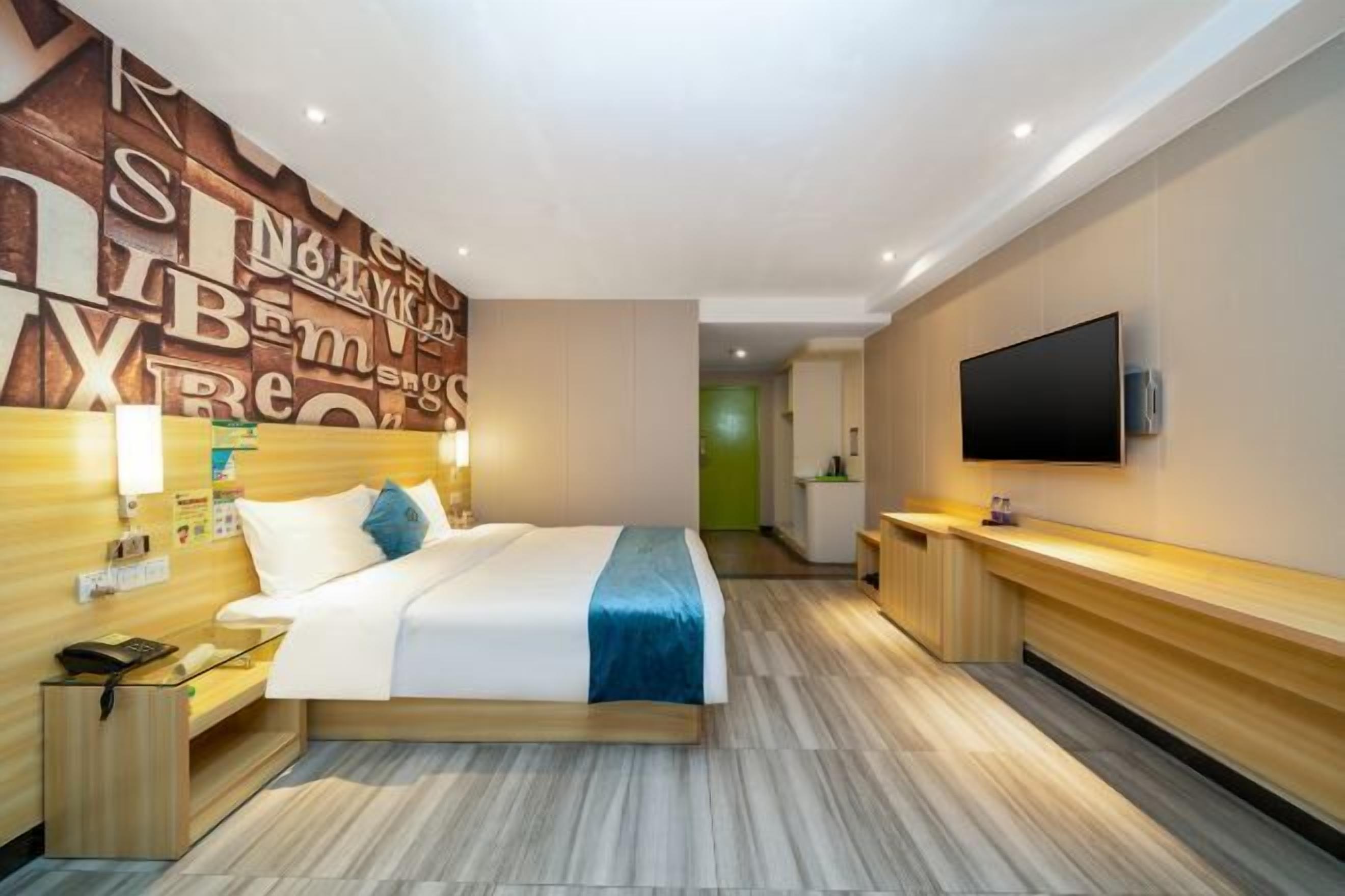A modern hotel room with a large bed, bedside table, and a flat-screen TV mounted on the wall.