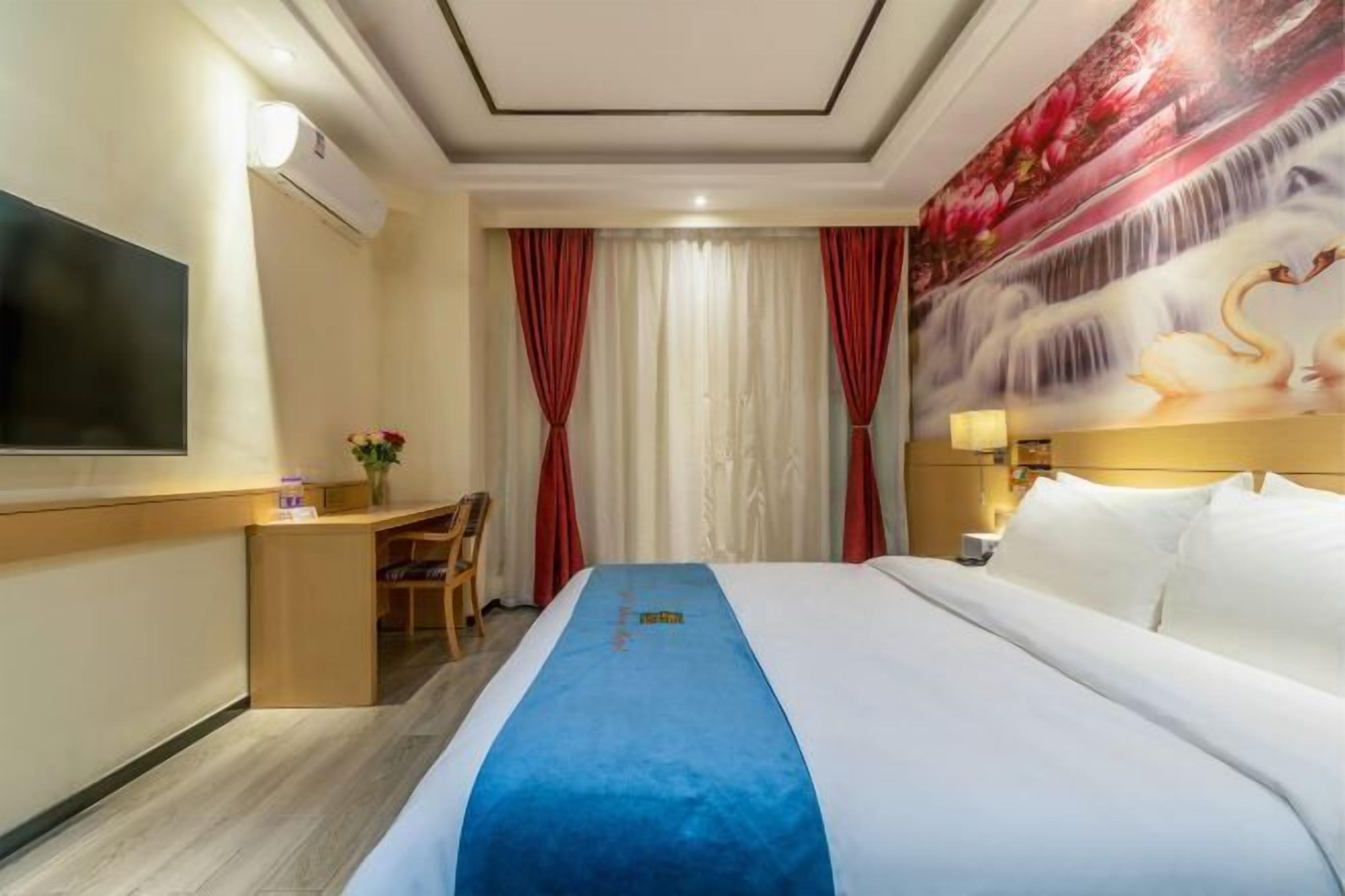 Una camera d'albergo con un letto grande, una scrivania, una televisione e un quadro di cigni appeso al muro.
