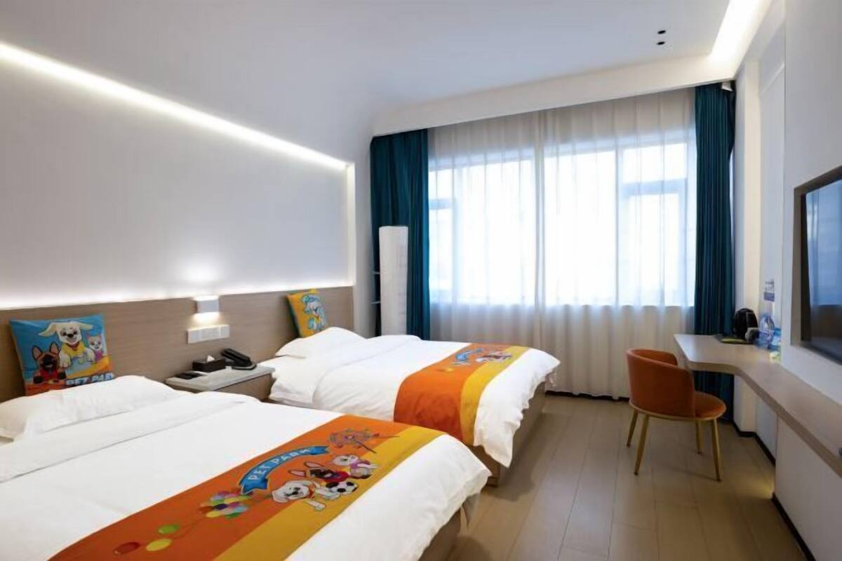 A hotel room with two beds, a desk, a chair, and a TV.