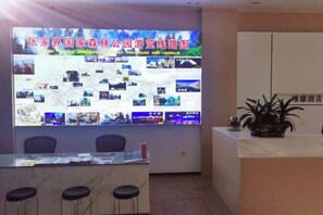 Zona de recepción con una gran pantalla digital, mostrador de recepción, taburetes de bar y una planta en maceta.