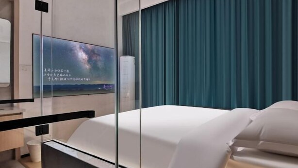 A modern hotel room with a large bed, a television mounted on the wall, and a view of the cityscape. - WeiKang Hotel JiShouDaXueDian (Zhangjiajie)