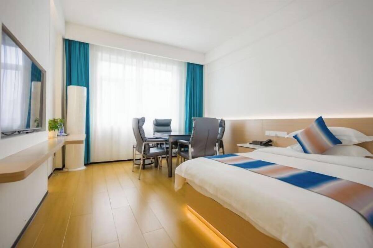 A hotel room with a bed, a desk, a chair, a TV, and a window with curtains.