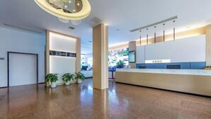A modern reception area with a reception desk, potted plants, and a clean, polished floor. - WeiKang Hotel JiShouDaXueDian (Zhangjiajie)