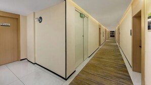 A hotel corridor with a tiled floor, a wooden door on the left, a glass door with a sign, and a carpeted floor. - WeiKang Hotel JiShouDaXueDian (Zhangjiajie)
