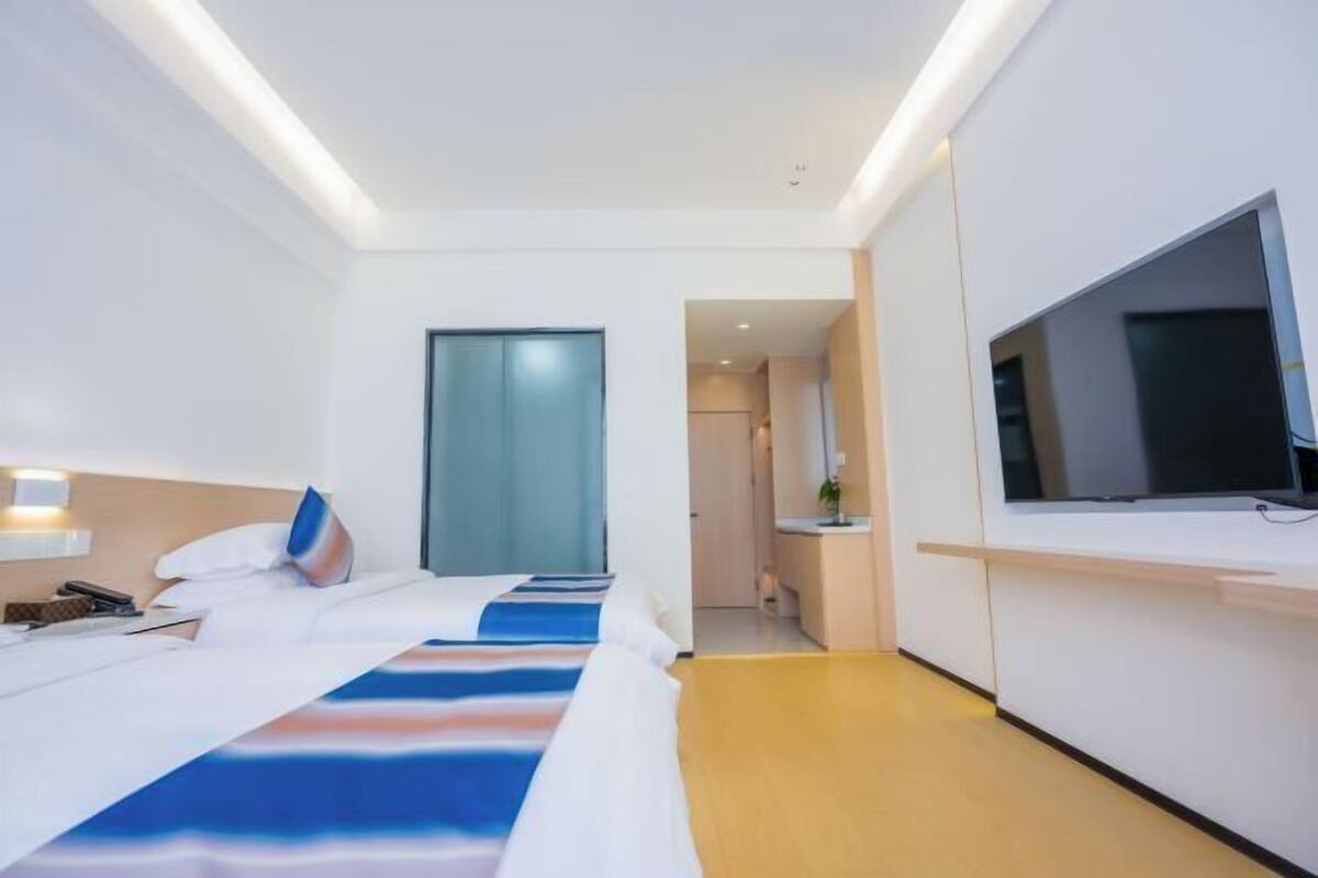 A hotel room with a bed, bedside table, TV, and a view of the hallway.