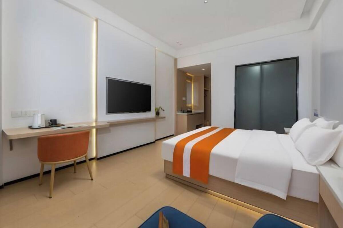 A modern hotel room with a bed, a desk, a chair, and a TV.