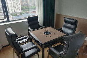A room with a table and four chairs, a window with a view of buildings, and a curtain. - WeiKang Hotel JiShouDaXueDian (Zhangjiajie)