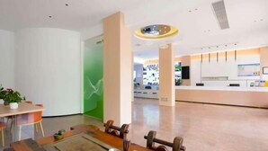A modern hotel lobby with a reception desk, a dining area with a wooden table, and a green accent wall. - WeiKang Hotel JiShouDaXueDian (Zhangjiajie)