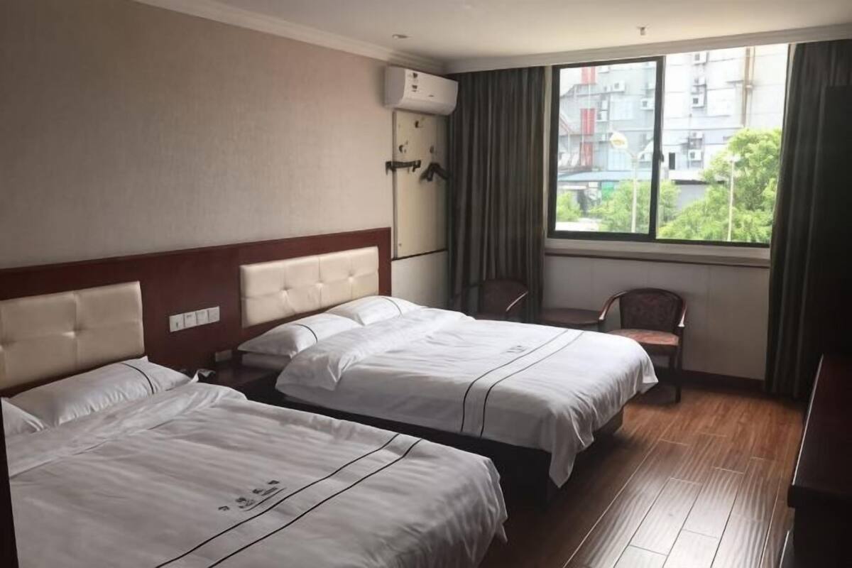 A hotel room with two beds, a window with a view of buildings, and a chair.