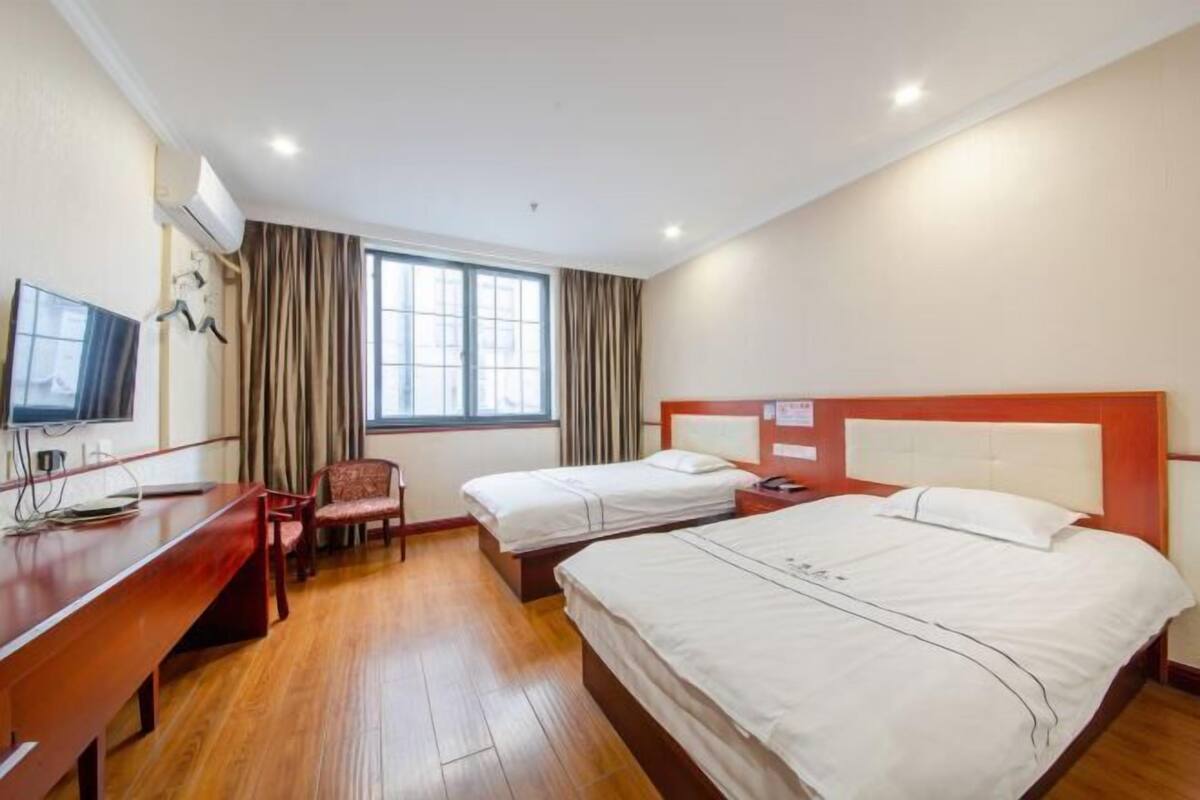 A hotel room with two beds, a desk, a chair, a television, and a window with curtains.