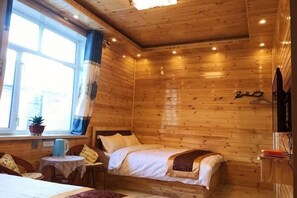 Una habitación de cabaña de madera con una cama, una mesita con una planta y una ventana con cortinas.