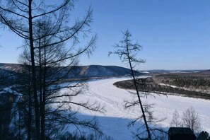 Un paysage enneigé avec une rivière, des arbres et des collines.