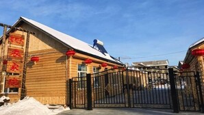 A wooden building with a snow-covered roof, a black gate, and red lanterns.