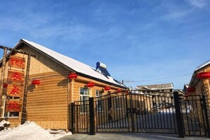Un edificio de madera con techo nevado, una verja negra y farolillos rojos.