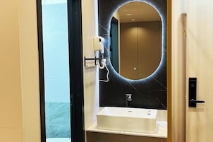 Un baño moderno con un espejo ovalado grande, un lavabo blanco y un secador de pelo montado en la pared.