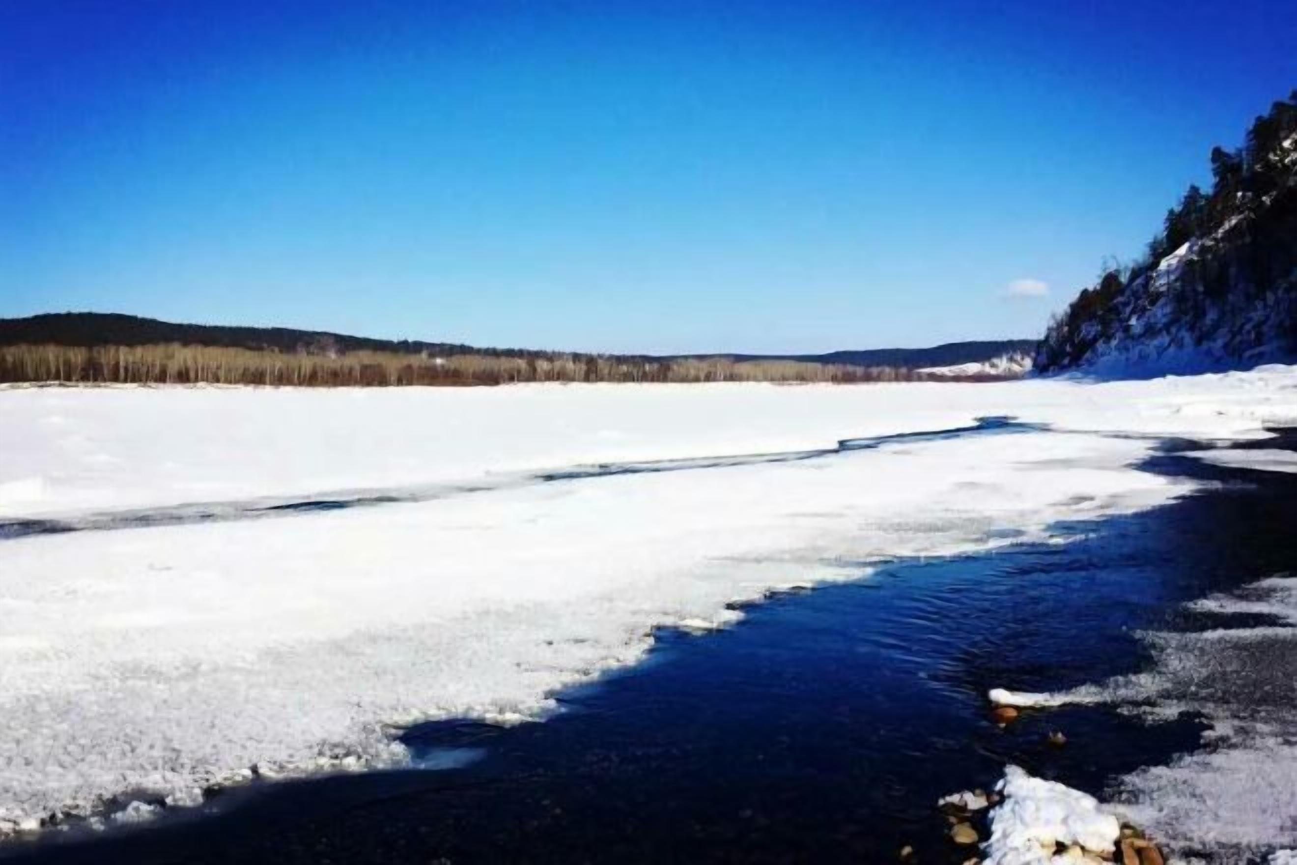 A frozen river with snow-covered banks and a clear blue sky.
