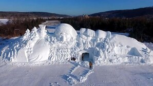 A snow sculpture with a tunnel entrance, surrounded by snow-covered terrain and distant hills.