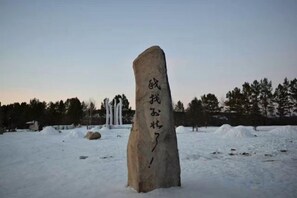 Een stenen monument met Japanse tekens in een besneeerd landschap met bomen op de achtergrond.