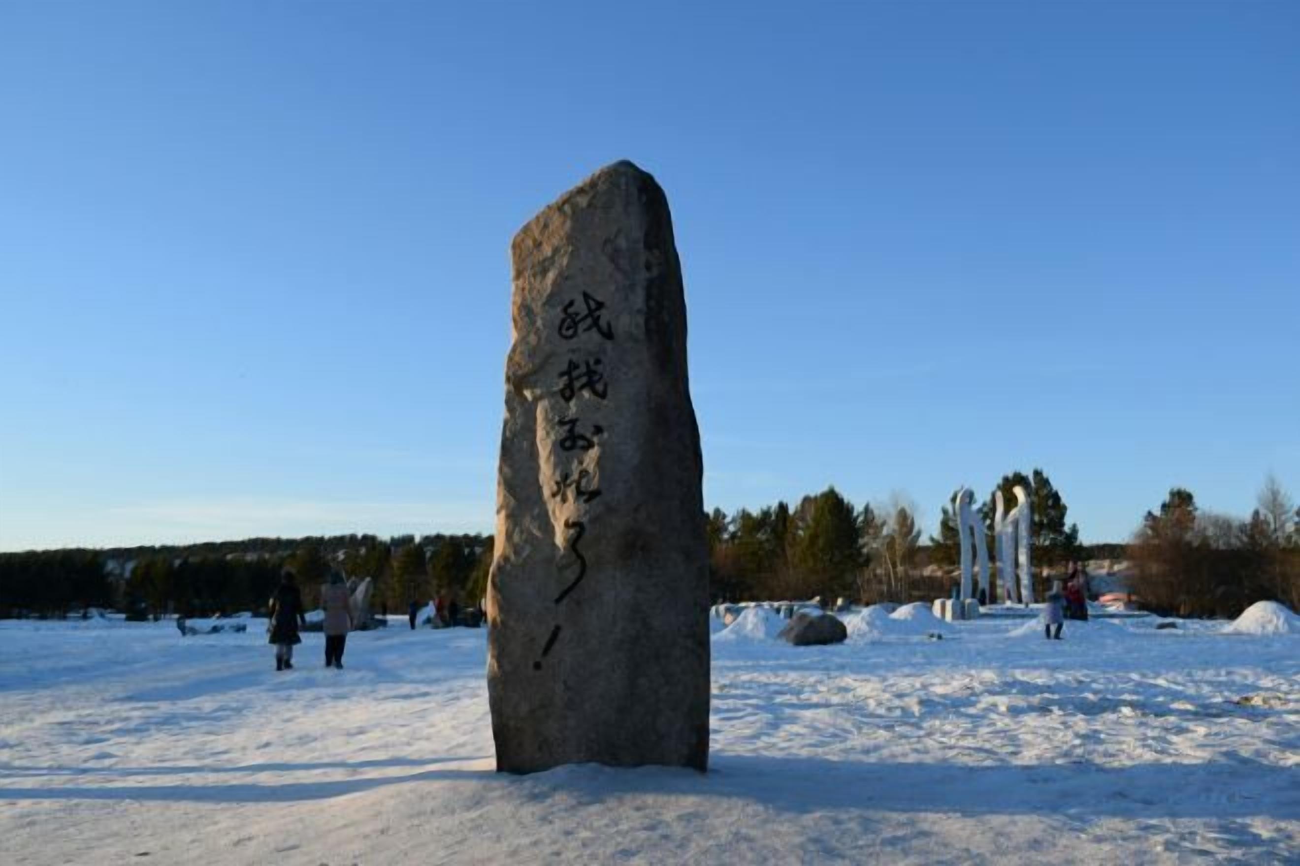A large standing stone with inscriptions, surrounded by snow and trees.