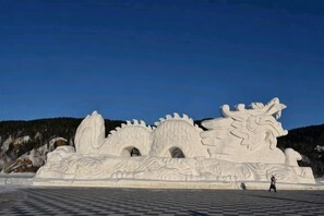 A large snow sculpture with intricate designs, a checkered ground, and a person walking in front. - Laocunzhang Farmhouse (Mohe)