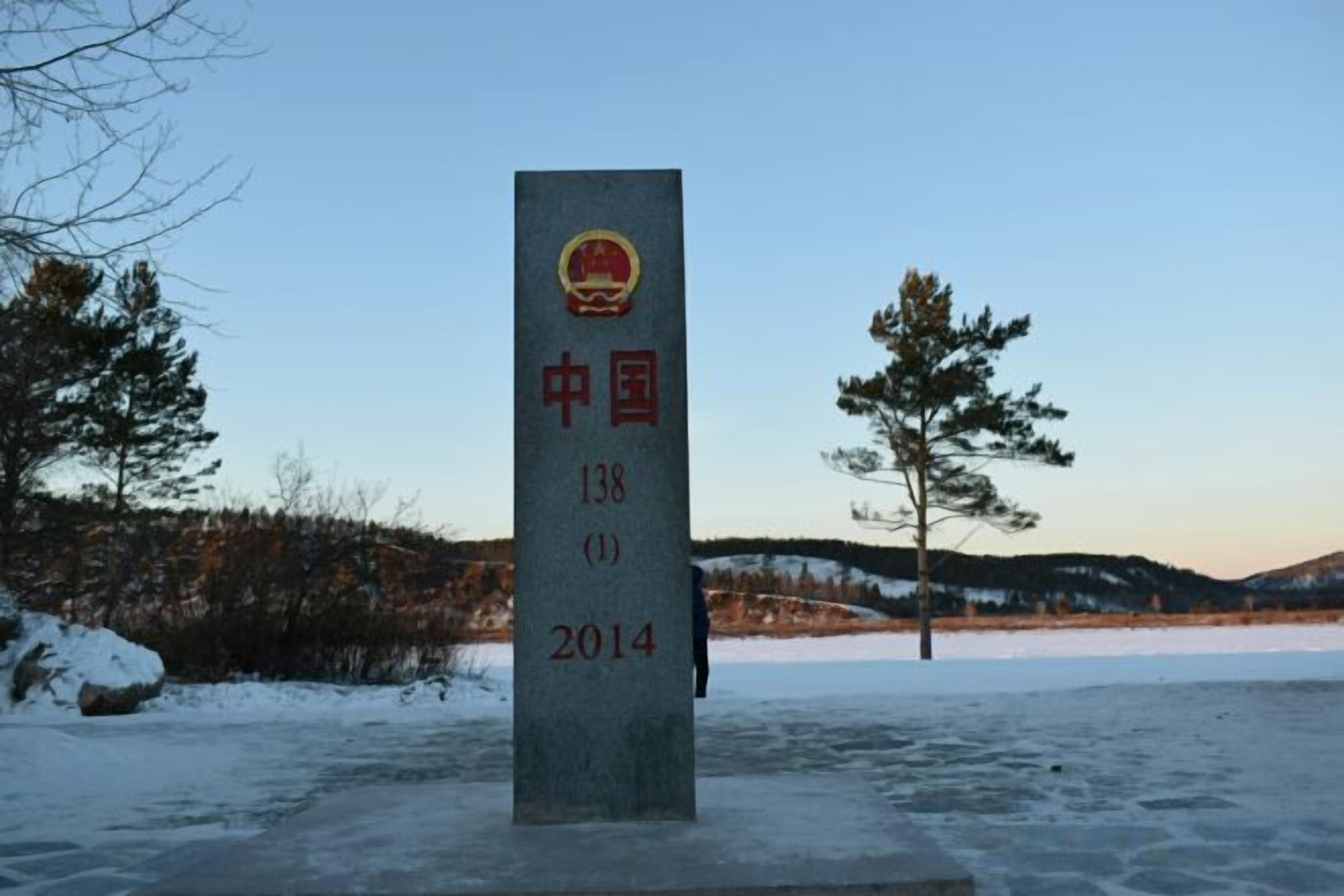 A monument with inscriptions, set against a winter landscape with trees and a clear sky.