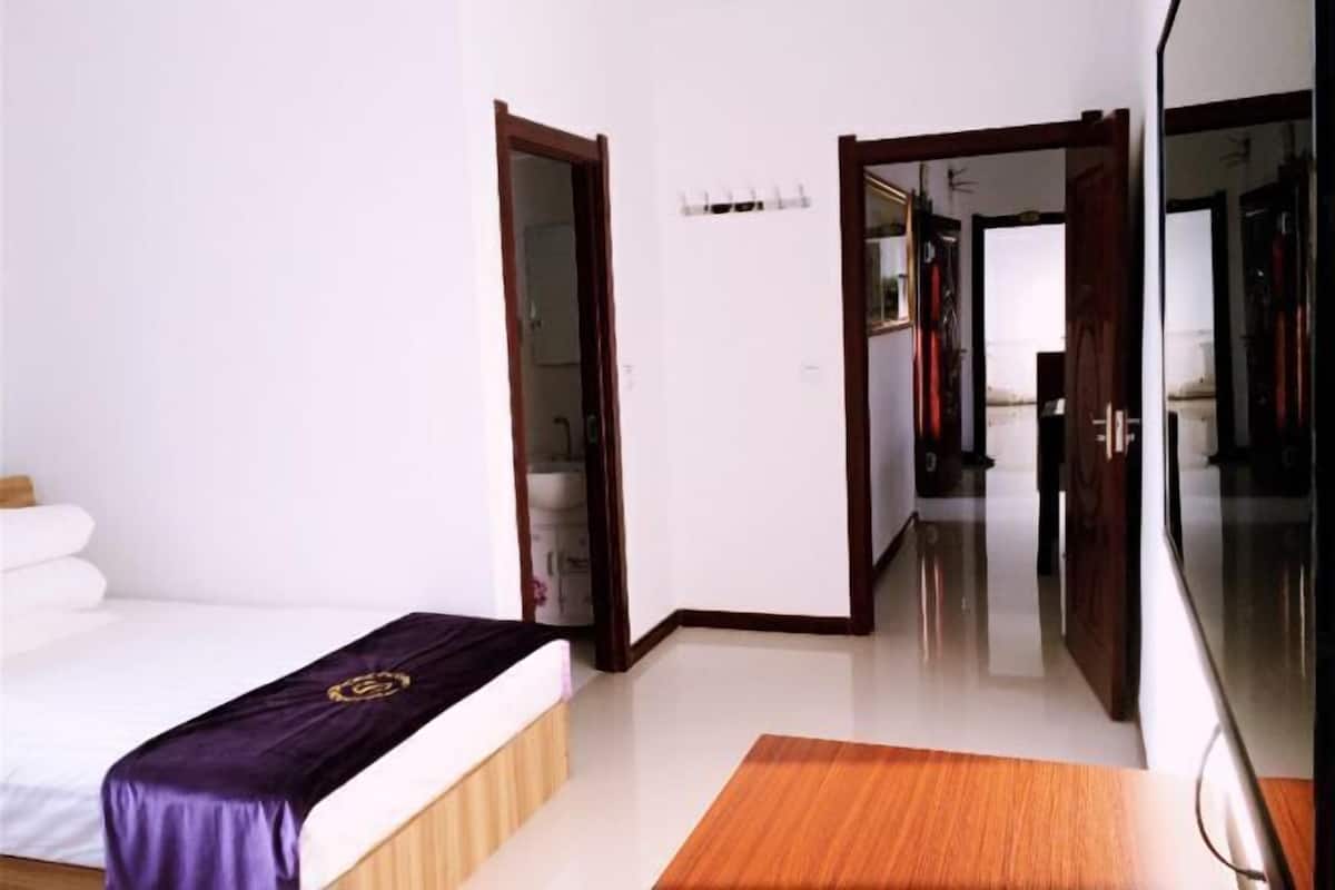 Ein Hotelzimmer mit Bett, Holzboden, Spiegel und einer Tür zu einem weiteren Raum.