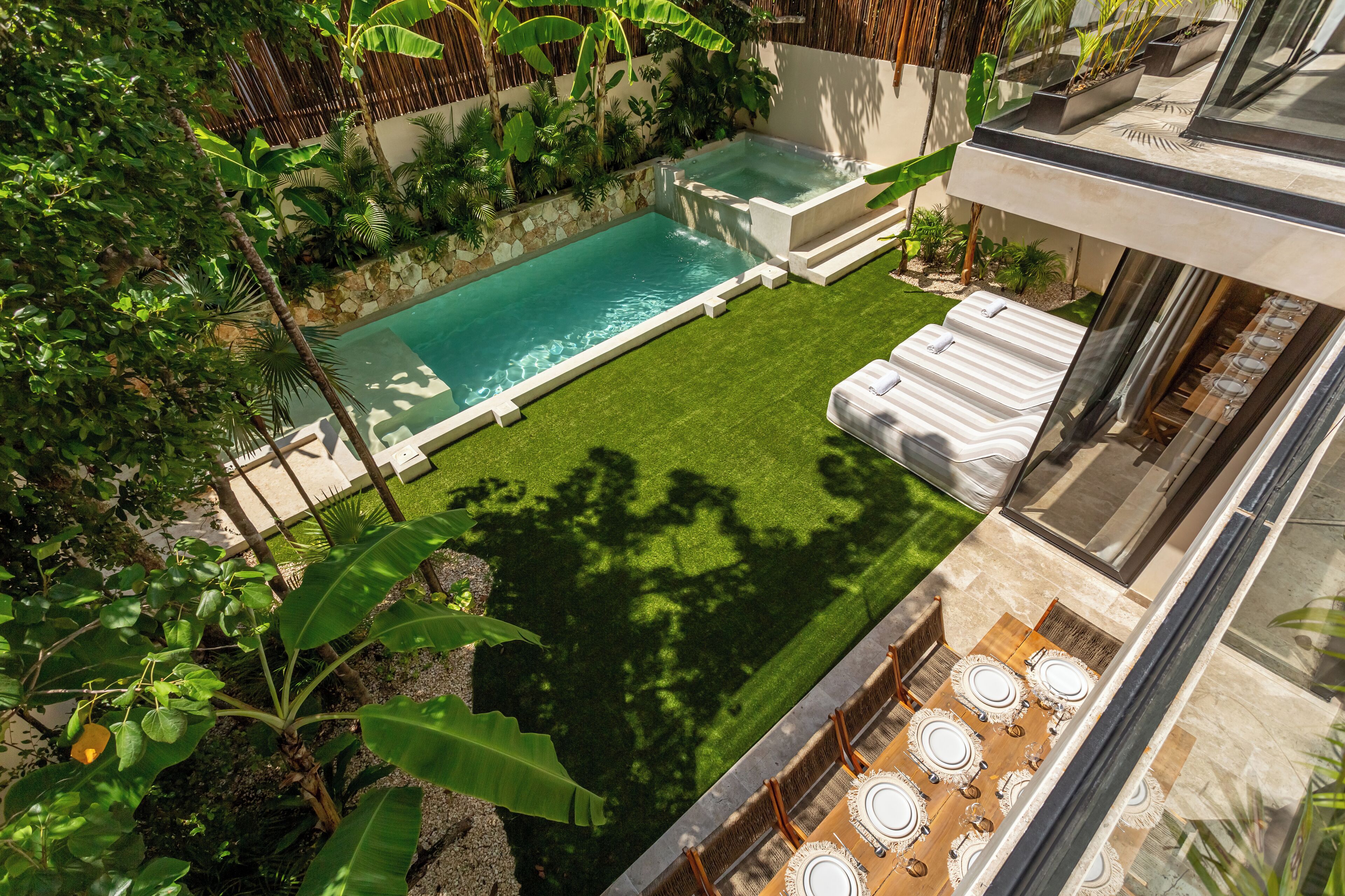 A rooftop pool with a glass balustrade, surrounded by lush greenery and a dining area with round tables and chairs.