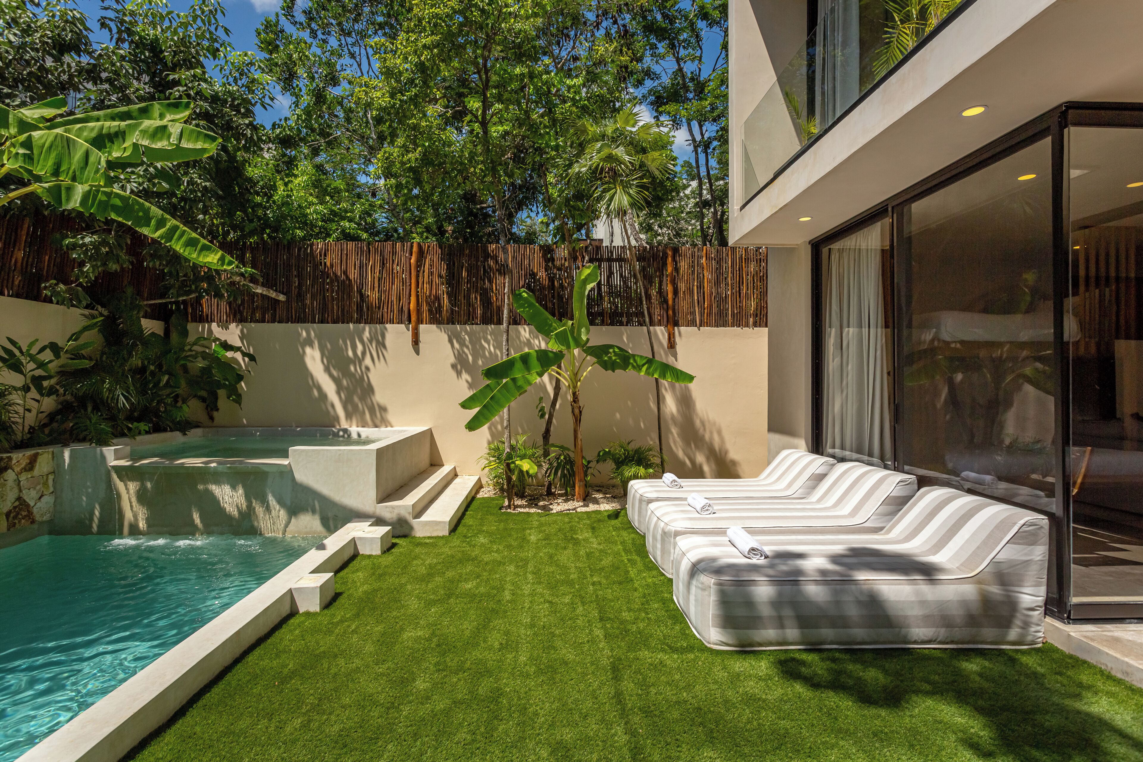 A modern outdoor pool area with a jacuzzi, a grassy lawn, and a seating area with white loungers.