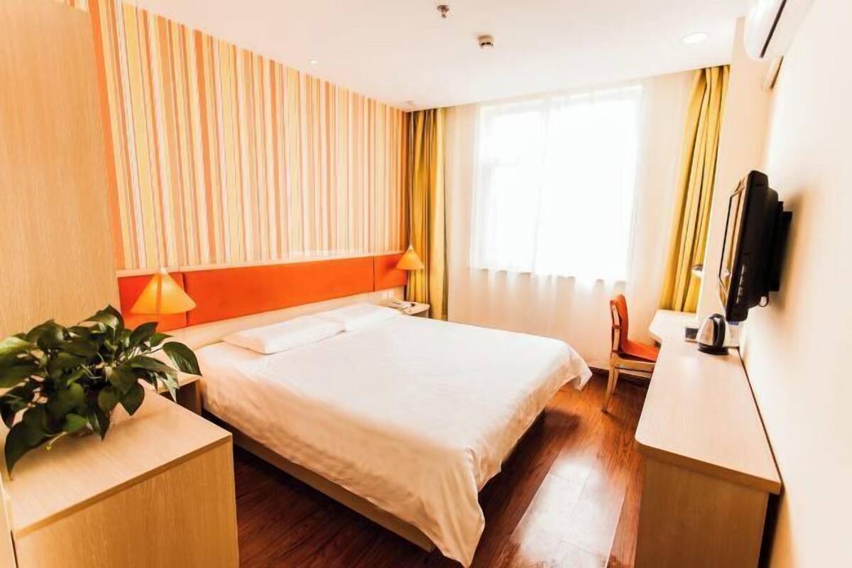 Habitació d'hotel amb llit, làmpades de nit, escriptori, cadira, televisió i finestra amb cortines.