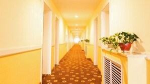 A hotel hallway with a patterned carpet, yellow walls, and potted plants. - Home Inn (Taiyuan Jinci Road Jinyang Lake Park) (Taiyuan)