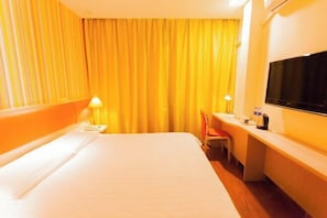 Une chambre d’hôtel avec un lit, un bureau, une chaise, une télévision et des rideaux.