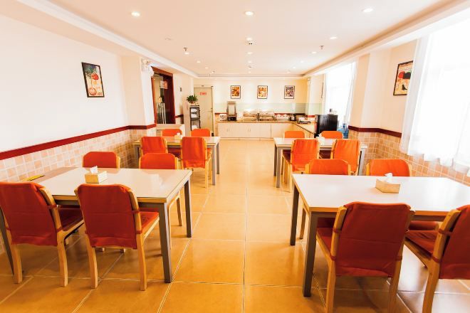 Un comedor con mesas y sillas, una cocina al fondo y un suelo de baldosas.