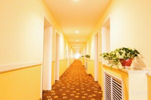 Um corredor de hotel com carpete estampado, paredes brancas e plantas em vasos.