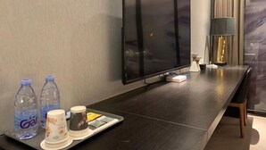 A modern hotel room with a flat-screen TV, water bottles, a tray with cups and a smartphone, and a lamp. - Joyous Hotel (Shanghai)