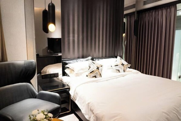 Ett modernt hotellrum med en stor säng, en sittgrupp med en fåtölj, ett sängbord och en väggmonterad TV.